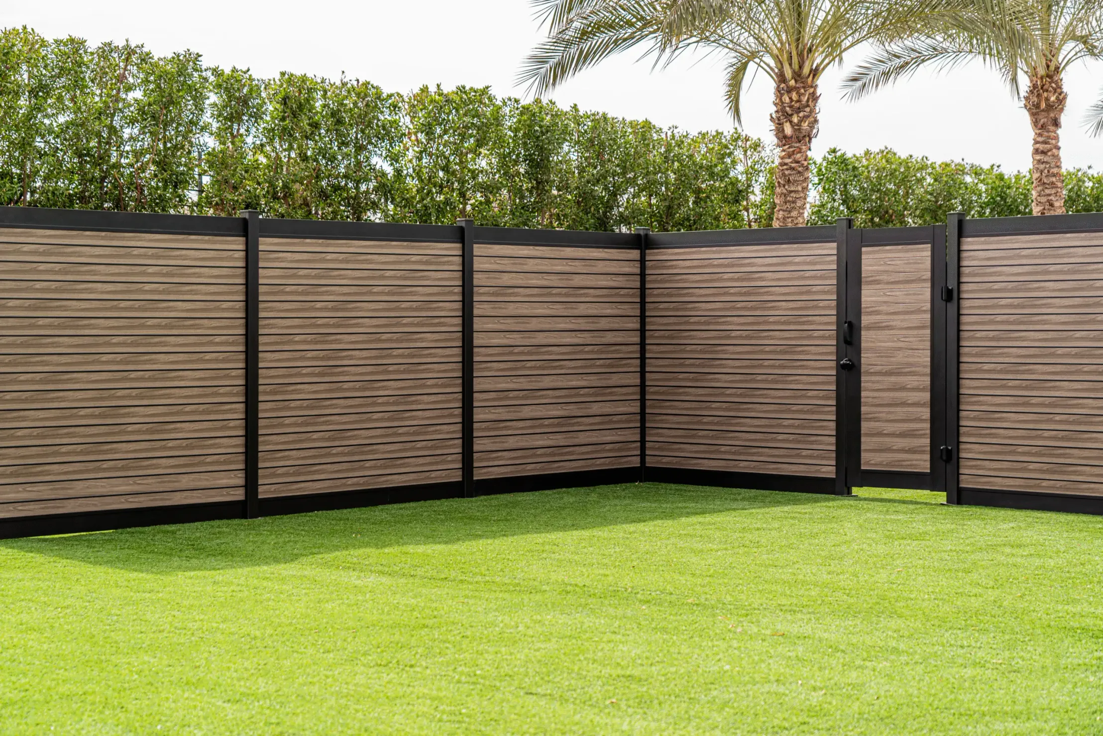 Wood-grain aluminum fence with an integrated swing gate enclosing a landscaped yard